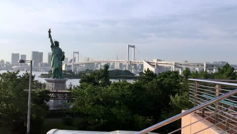 Odaiba-Statue-of-Liberty-replica-in-Minato-City-with-suspension-Rainbow-Bridge-in-the-background,-Handheld-Shot