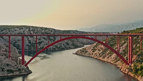 wide-aerial-shot-of-a-big-red-bridge-on-a-beautiful-mountain-scenery-on-sunset,-vertigo-effect