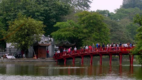 Huc-red-bridge-also-called-the-sunshine-bridge-at-the-Ngoc-Son-temple-with-tourists-crossing-it,-Locked-establishing-shot