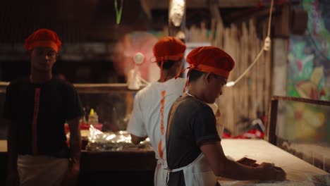 Equipos-De-Cocina-Masculinos-Con-Tocados-Rojos-Y-Delantales-Ocupados-Preparando-Comida-En-Un-Restaurante-En-El-Nido,-Filipinas---Primer-Plano