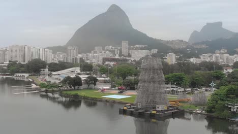 Aerial-pan-showing-the-partly-constructed-floating-Christmas-tree-on-the-shore-of-the-city-lake-in-Rio-de-Janeiro-on-a-hazy-early-morning-with-the-Two-Brothers-mountain-in-the-background