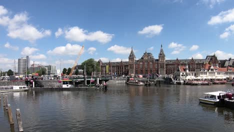 Viel-Bootsaktivität-Auf-Den-Kanälen-Und-Amsterdamer-Hauptbahnhof-Im-Hintergrund-An-Einem-Schönen-Sommertag,-Niederlande