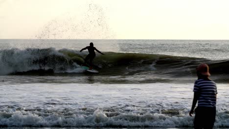 Surfer-catching-and-riding-a-large-wave-during-sundown-camera-follows-him,-right-tracking-shot