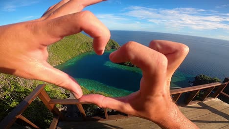 POV-perspective-of-a-man-looking-out-over-a-heart-shaped-lagoon-and-forming-a-heart-with-his-hands