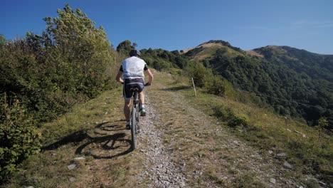 Un-Ciclista-Masculino-En-Forma-Monta-Una-Bicicleta-De-Montaña-Cuesta-Arriba-En-Un-Día-Soleado-De-Verano,-Cielos-Despejados-Y-Un-Clima-Hermoso