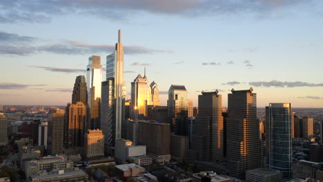Aerial-drone-fly-away-view-of-the-downtown-Philadelphia-skyline-featuring-tall,-glass-skyscrapers-at-sunset-with-gold-and-purple-light-showing-the-Comcast-Technology-Center