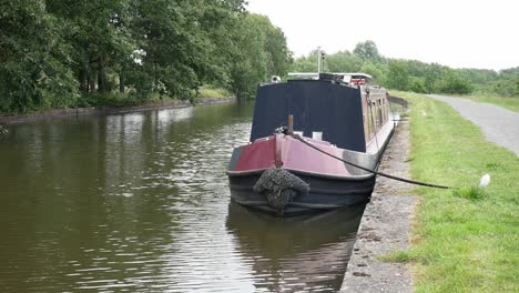 British-long-canal-narrow-boat-moored-along-scenic-English-marine-countryside-waterway-path