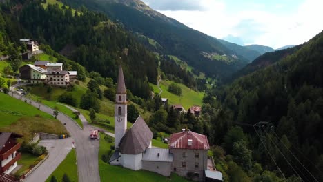 Village-with-road-and-church-in-the-mountain-area-with-houses-and-chalets,-Aerial-drone-orbit-shot