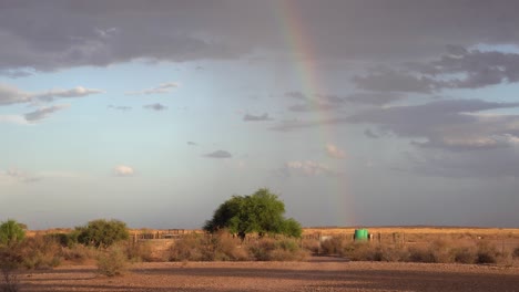 Still-stable-shot-of-a-rainbow-in-the-distance,-with-a-sheep-enclosure-in-front-on-a-sheep-farm-in-Namibia