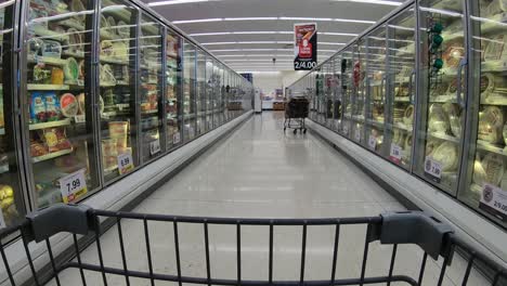 POV-from-the-shopping-cart-while-going-past-the-frozen-food-freezers-filled-with-ice-cream-and-pizza-at-the-grocery-store