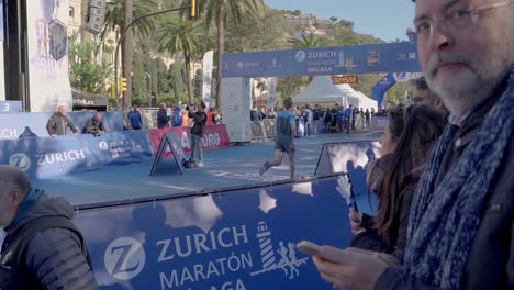 Marathon-runner-crosses-the-finish-line,-clock-showing-under-three-hours,-camera-follows-action,-Malaga,-Spain