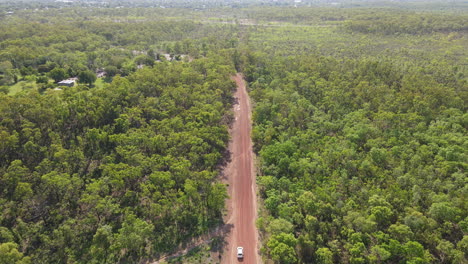 High-Slow-moving-Aerial-Drone-shot-of-Following-Car-Driving-on-Long-Straight-Red-Road-and-Green-Bushland-Near-Holmes-Jungle-Nature-Park,-Darwin,-Northern-Territory
