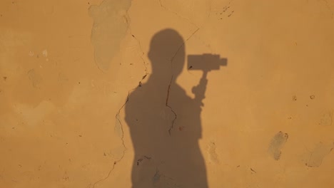 Abstract-view-of-shade-man-holding-gimbal-reflected-on-yellow-cracked-wall