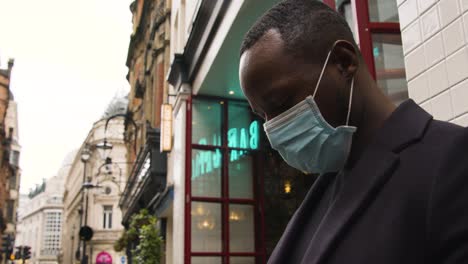 Male-wearing-a-medical-mask-looking-around-a-busy-street-in-London-low-angle
