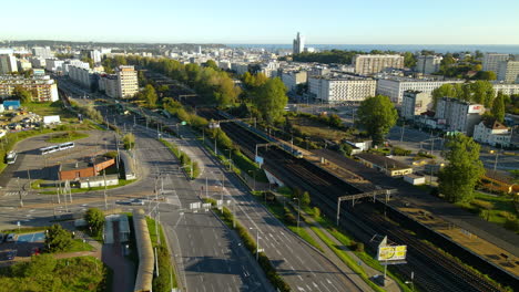 Aerial-flyover-Gdynia-City-during-sunny-day-with-driving-cars-on-main-road-and-train-on-rails,Poland