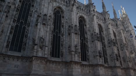 Duomo-di-Milano-cathedral-side-wall-exterior,-wide-shot-pan-left-tilt-up-during-bright-sunny-day