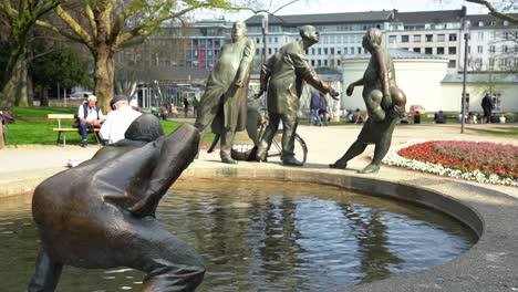 Bronze-statue-with-people-and-whirl-pool-in-Aachen,-Germany,-called-Circulation-of-Money-with-the-Elisenbrunnen-in-background