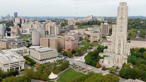 University-of-Pittsburgh,-aerial-establishing-shot-of-Cathedral-of-Learning,-academic-buildings,-dorms,-and-urban-city-skyline-in-distance,-Pennsylvania,-USA
