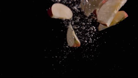 Apple-Slices-Falling-into-Water-Super-Slowmotion,-Black-Background,-lots-of-Air-Bubbles,-4k240fps