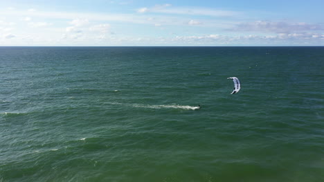 AERIAL:-Locked-Shot-of-Surfer-Passing-By-with-Power-Kite-Alongside-Blue-Sky-in-Background