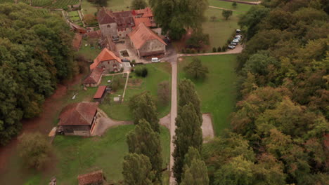 Aerial-of-small-road-in-countryside,-tilting-up-to-reveal-old-buildings-near-lake