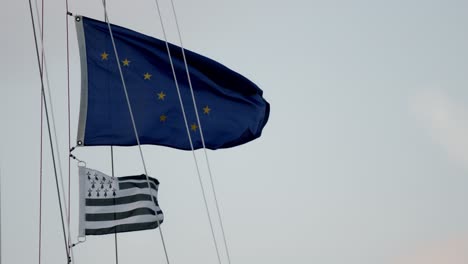 Flaggen-Von-Alaska-Und-Der-Französischen-Region-Bretagne-Wehen-An-Seilen-Eines-Segelboots,-Das-Im-Hafen-Vor-Anker-Liegt,-Aus-Nächster-Nähe