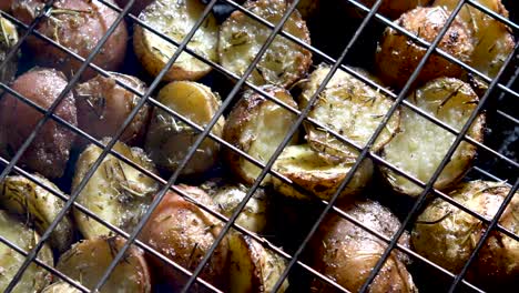 Camera-looking-straight-down-and-panning-across-browned-herbed-new-potatoes-in-a-wire-basket-on-a-hot-grill-with-red-embers-glowing-beneath