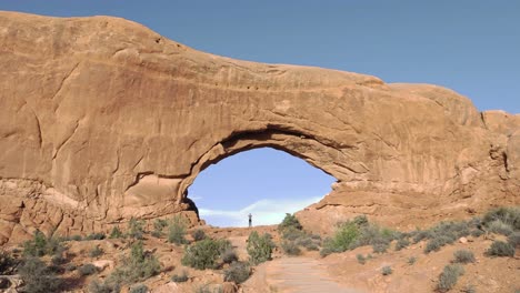Tiny-person-standing-inside-North-Window-in-Arches-National-Park,-Utah---slow-motion
