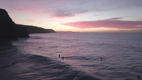 Sonnenuntergangsurfer-Und-Silhouettenklippen-In-Cornwall