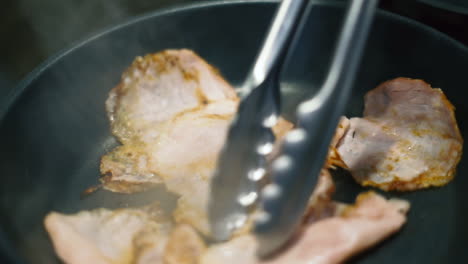 Grilling-ham-slices-in-a-black-pan,-flipped-with-metal-tongs