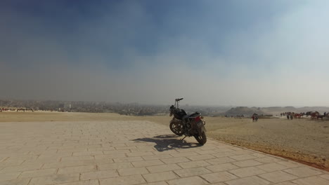 Camera-going-towards-a-motorbike-standing-in-front-of-an-astonishing-panoramic-view-of-the-Egyptian-desert-during-a-sunny-day-in-Giza
