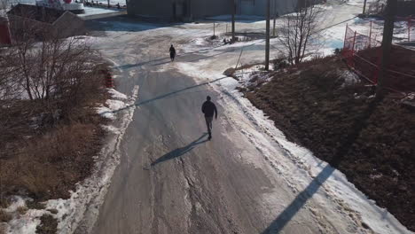 Man-walking-behind-woman-downhill-towards-a-snowy-road-towards-a-frozen-dock-in-Winter