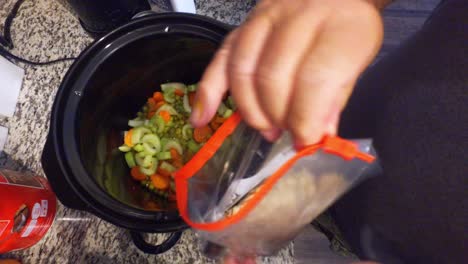 cooking-a-stew-in-a-slow-cooker-looking-down-into-the-pot-and-stirring-the-peas-carrots-and-other-ingredients