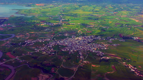 Explore-the-charming-village,-Aerial-view-covered-with-green-farms,-narrow-streets-and-a-wriggling-river-side-of-the-valley