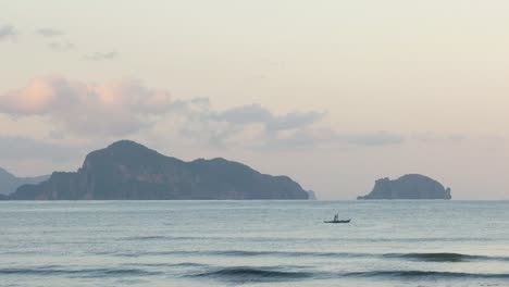 Slow-motion-shot-of-paddling-man-in-boat-in-front-of-limestone-cliffs-at-dusk-seen-from-beach