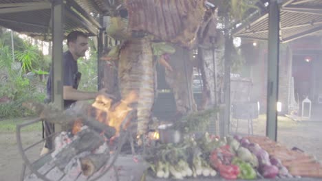 Slow-motion-handheld-shot-of-a-chef-adding-carbon-to-the-fireplace-cooking-grilled-vegetables-and-meat-on-a-typical-argentinian-barbecue-called-asado