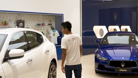 Young-Asian-male-walking-into-luxury-shopping-mall-Maserati-dealership-to-view-choice-of-vehicles-in-Icon-Siam,-Bangkok,-Thailand