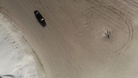 Top-down-view-of-the-beach-and-dunes,-turning-left-and-following-a-truck-driving-on-the-beach