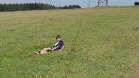 Young-boy-run-and-fall-in-green-field---tracking-shot