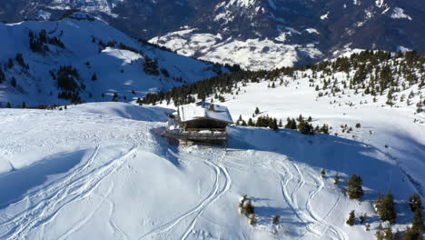 Aerial-view-panning-around-a-mountain-top-chalet-in-the-snow-on-a-sunny-day