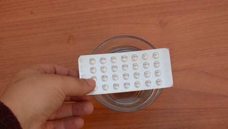 woman-taking-contraceptive-pills-from-the-top-of-the-glass-of-water-on-the-wooden-table