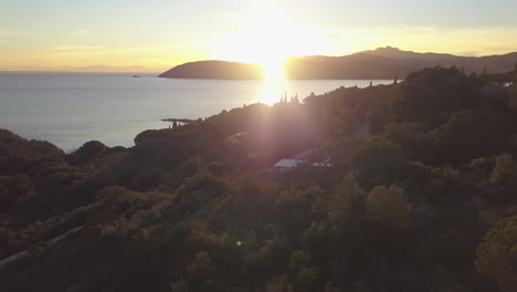 Luftdrohnenaufnahme-Rückwärts-über-Solarbetriebenes-Haus-Und-Bäume,-Die-Alle-Während-Des-Sonnenuntergangs-In-Elba,-Italien,-Von-Goldenem-Sonnenlicht-Bedeckt-Sind