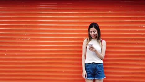 Zeitlupe:-Schönes-Junges-Mädchen-Benutzt-Smartphone-Vor-Orangefarbenem,-Rotem-Hintergrund