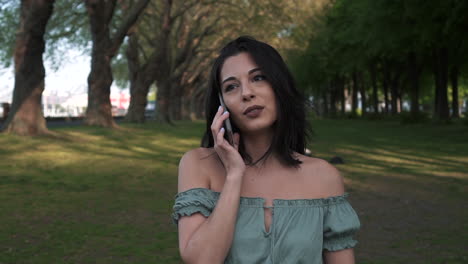 Portrait-of-smiling-woman-using-smartphone-to-make-a-call-while-walking-in-a-beautiful-park-in-London