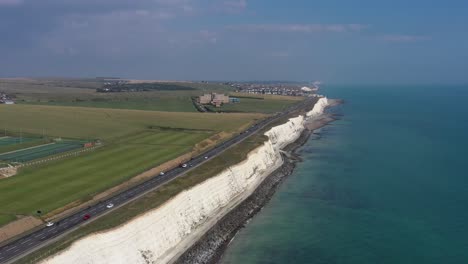 Wide-aerial-view-tracking-traffic-along-the-A259-coast-road-near-Brighton,-with-the-Blind-Veterans-UK-building-near-Rottingdean,-Chalk-cliffs-and-coastline