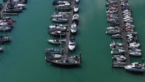 Aerial-push-over---pan-down-to-a-jetty-with-moored-yachts---sailing-boats,-with-men-discussing-boating-life,-shot-at-Brighton-Marina,-UK