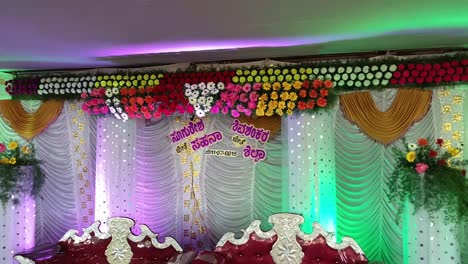 Drone-shot-of-a-decorated-Indian-wedding-stage-with-chairs,-colorful-lightings,-and-flowers
