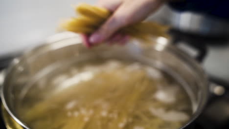 Cook-breaking-spaghetti-noodles-and-dropping-them-into-a-pot-in-slow-motion