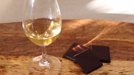 Zooming-out-from-a-closeup-of-a-glass-of-single-malt-scotch-whisky,-paired-with-squares-of-dark-chocolate-sitting-on-a-wooden-platter,-with-evening-sunlight-and-shadows