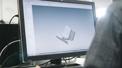 A-male-engineer-reviewing-a-3D-printed-product-while-watching-the-animated-3d-version-on-his-computer
